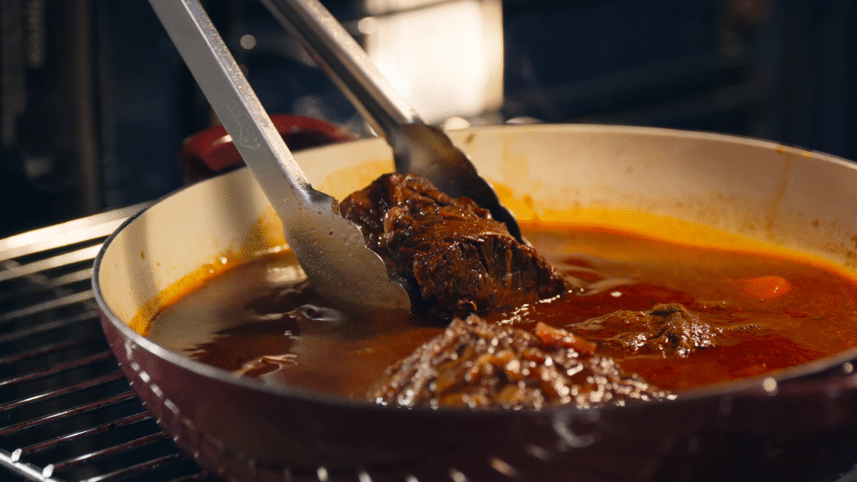 Nick DiGiovanni adding seared beef chuck to a Dutch oven with vegetables and sauce.