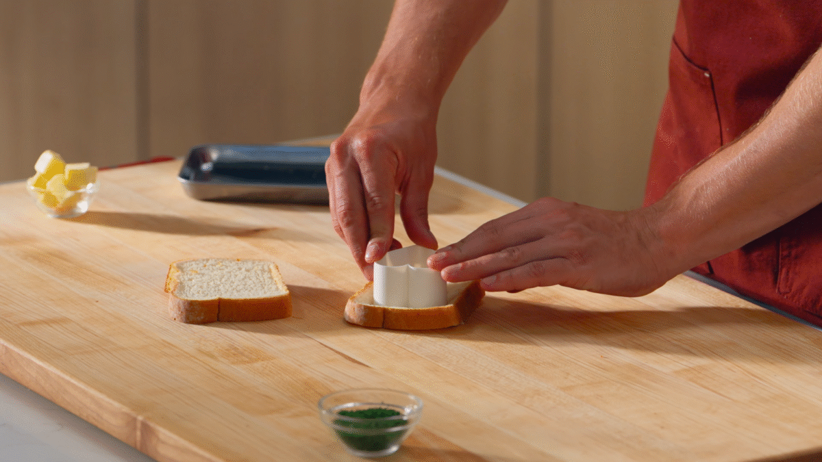 Nick DiGiovanni using a heart-shaped cookie cutter to cut white pieces of bread.