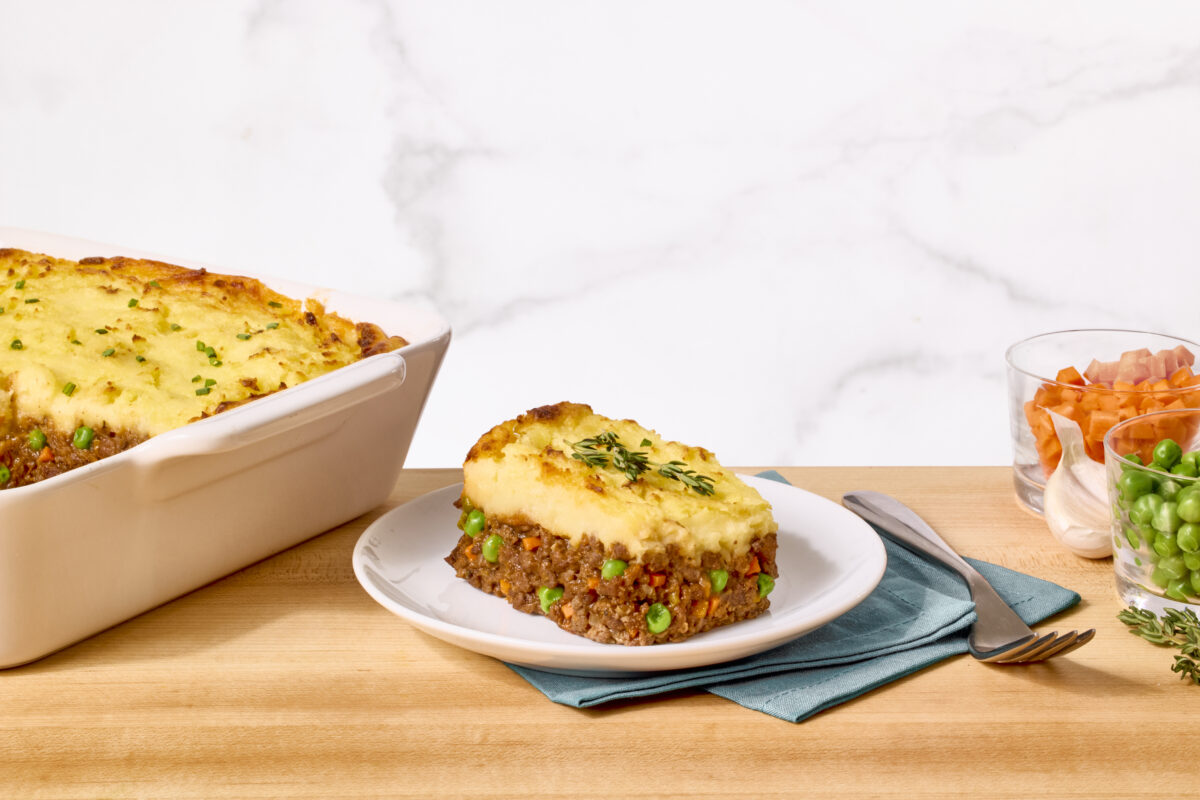 A serving of shepherd's pie on a plate next to a casserole dish of shepherd's pie and vegetables.