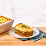 A serving of shepherd's pie on a plate next to a casserole dish of shepherd's pie and vegetables.