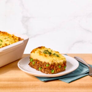 A serving of shepherd's pie on a plate next to a casserole dish of shepherd's pie and vegetables.
