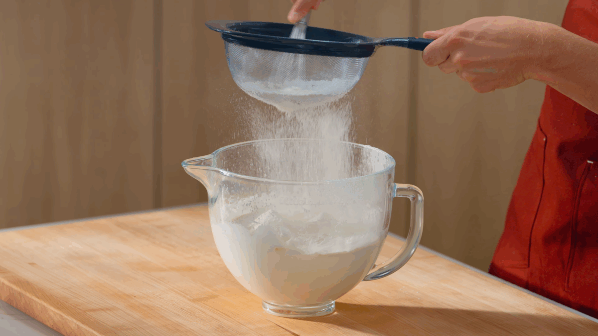 Nick DiGiovanni sifting dry ingredients into a bowl of meringue to make ladyfingers. 