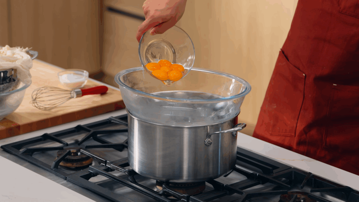 Nick DiGiovanni pouring egg yolks into a bowl set over a pot of boiling water. 