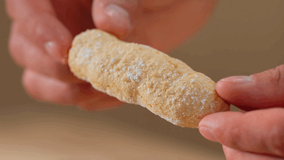 Nick DiGiovanni holding a homemade ladyfinger cookie dusted with powdered sugar. 