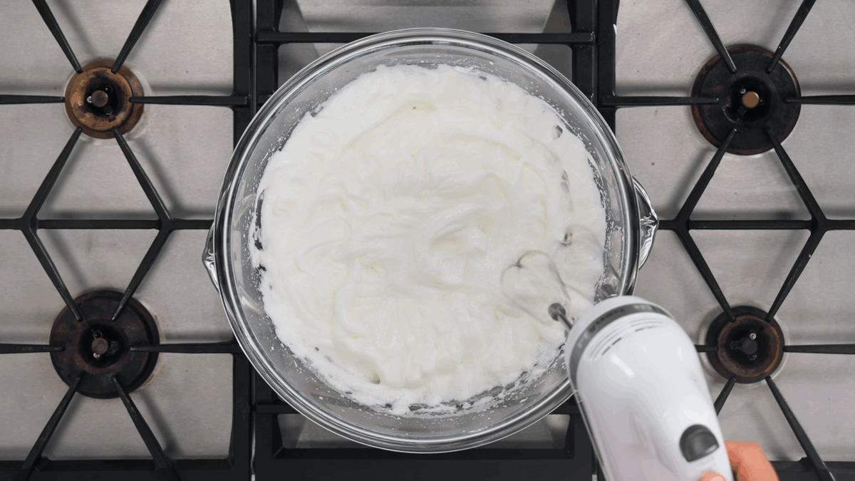 Nick DiGiovanni using an electric hand mixer to whip egg whites in a double boiler. 