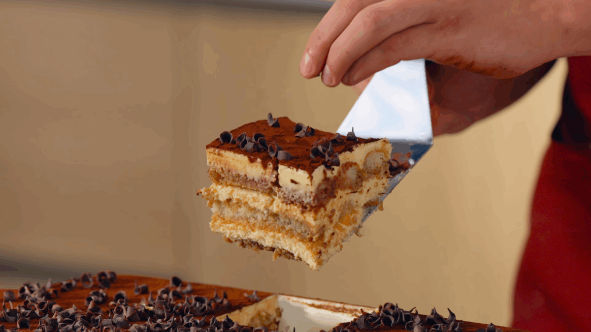 Nick DiGiovanni lifting a slice of homemade tiramisu topped with chocolate curls from a baking dish. 