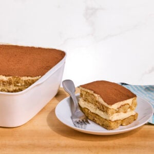 A dish of tiramisu with one serving missing and served on a plate.