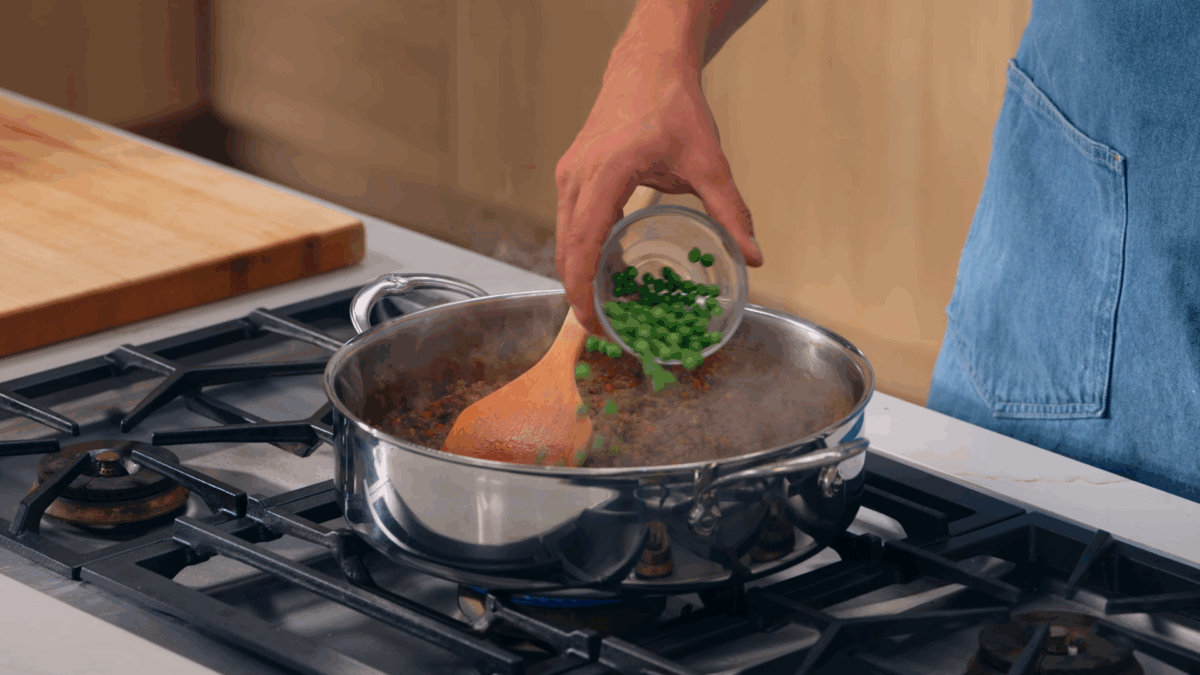 Nick DiGiovanni adding frozen peas to a sauté pan of shepherd's pie filling.