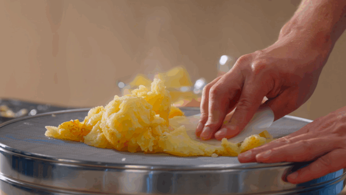 Nick DiGiovanni pushing baked potatoes through a drum sieve.