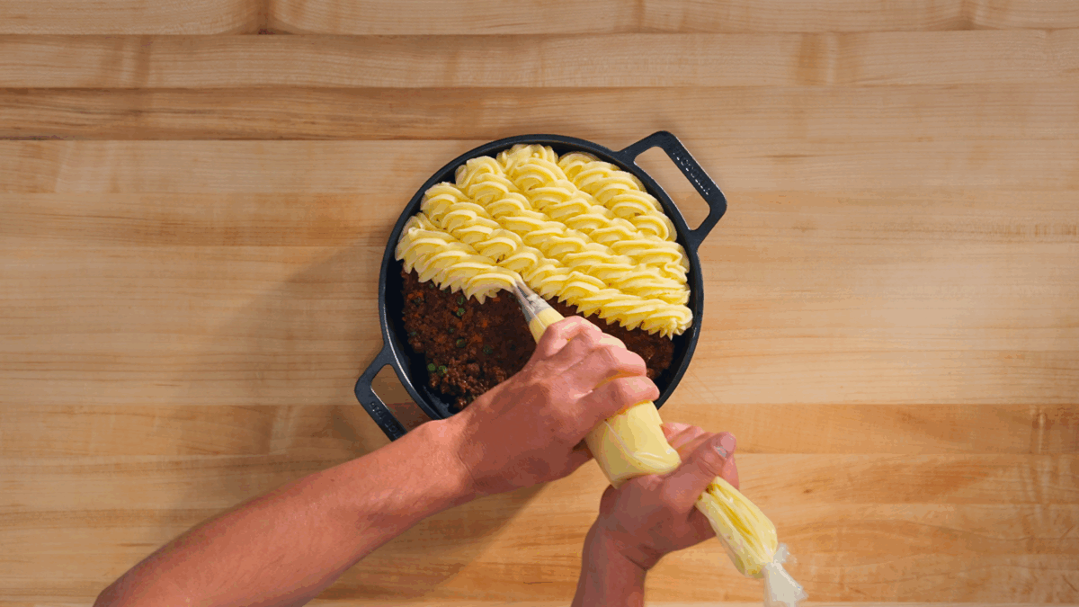 Nick DiGiovanni piping mashed potatoes onto shepherd's pie filling.