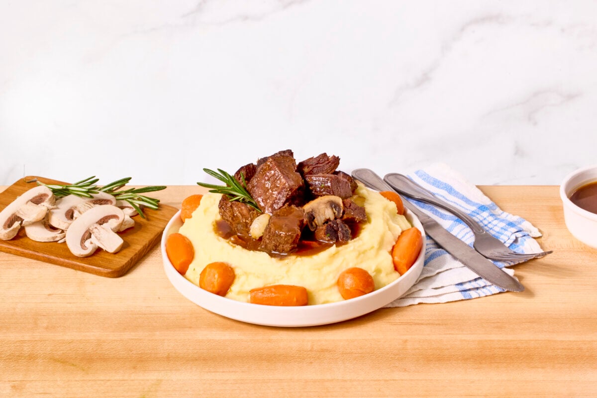 Beef bourguignon served on a plate over mashed potatoes with carrots around the edges.