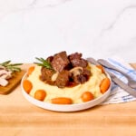 Beef bourguignon served on a plate over mashed potatoes with carrots around the edges.
